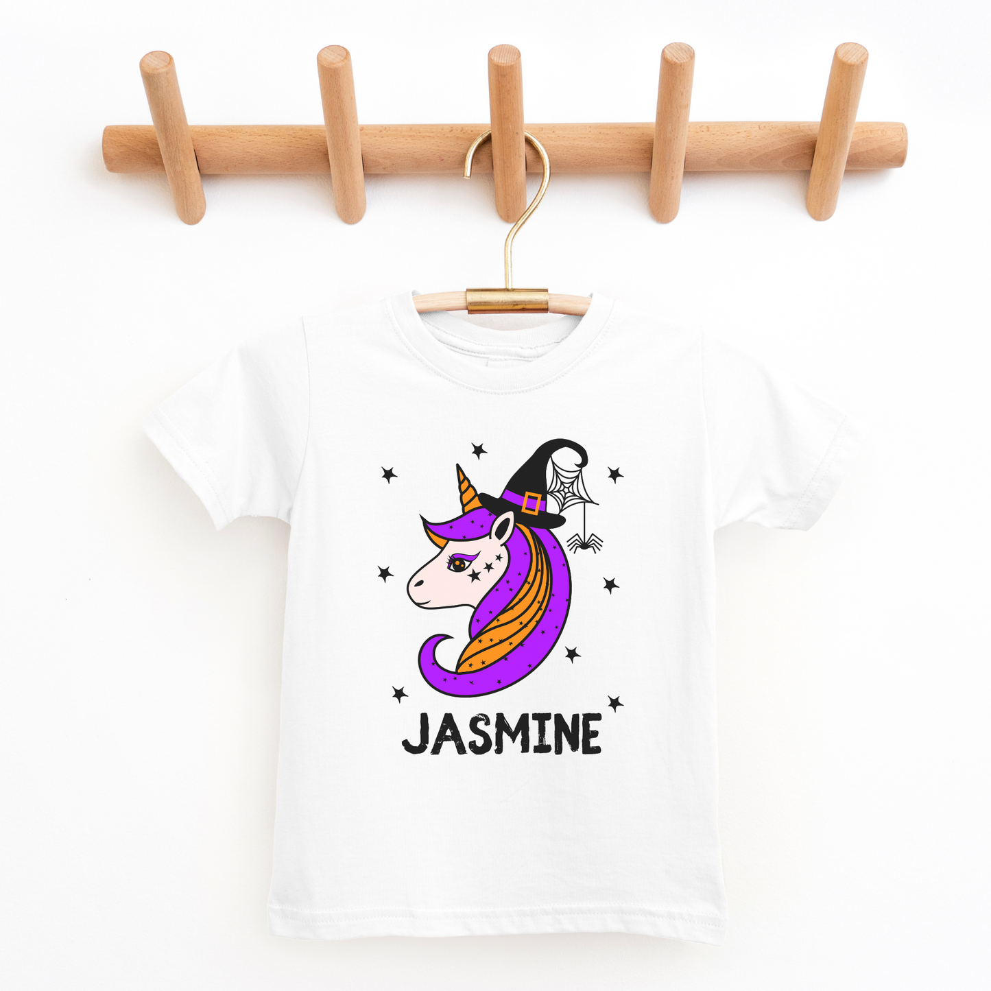Kids white t-shirt with a colourful Halloween unicorn design featuring a witch hat, spider web, and stars. Personalised with the name “Jasmine” printed below.