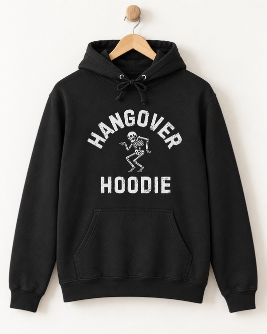 A black pullover hoodie hanging on a wooden hanger against a plain white wall. The hoodie features a white graphic print on the front with the words 'HANGOVER HOODIE' and a small dancing skeleton.