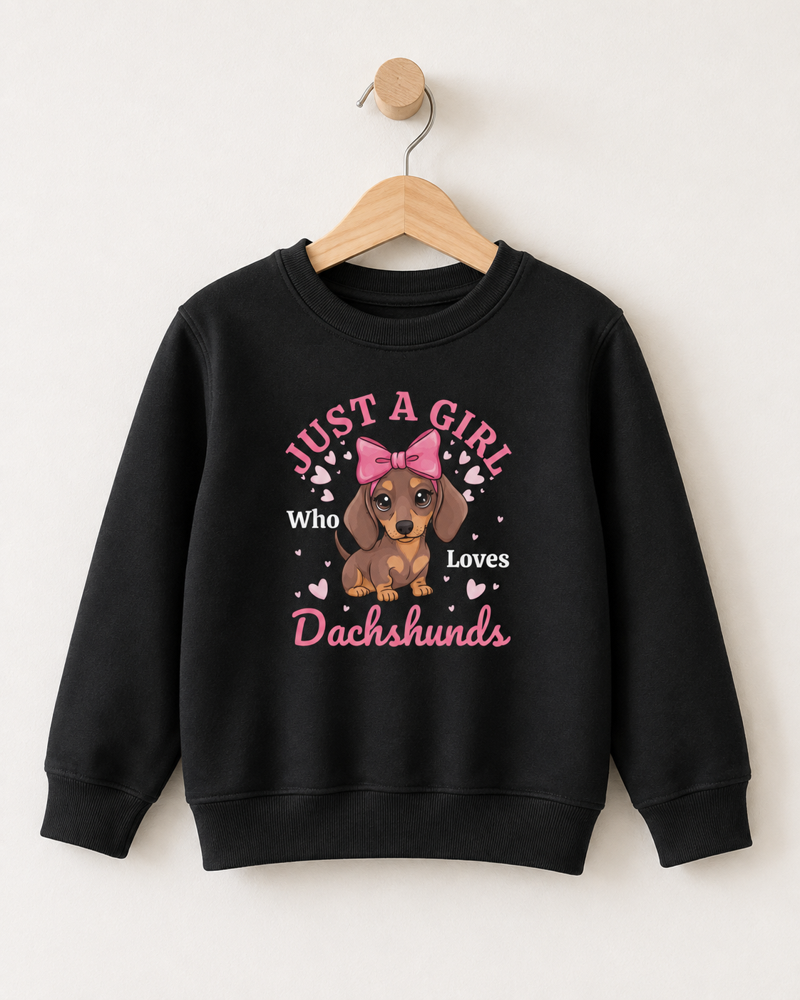 Black girls sweatshirt on a wooden hanger featuring a cute brown dachshund with a large pink bow, surrounded by pink hearts and “Just a Girl Who Loves Dachshunds” text.