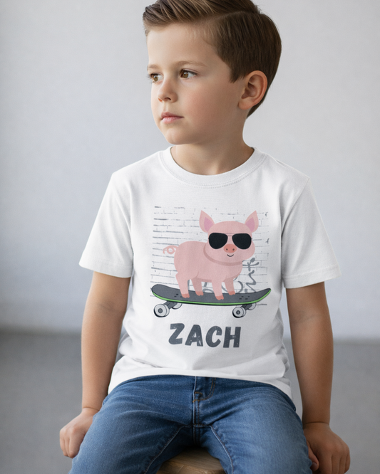 Boy sitting on wooden stool wearing custom name skateboarding pig kids t-shirt, indoor studio background, graphic fully visible