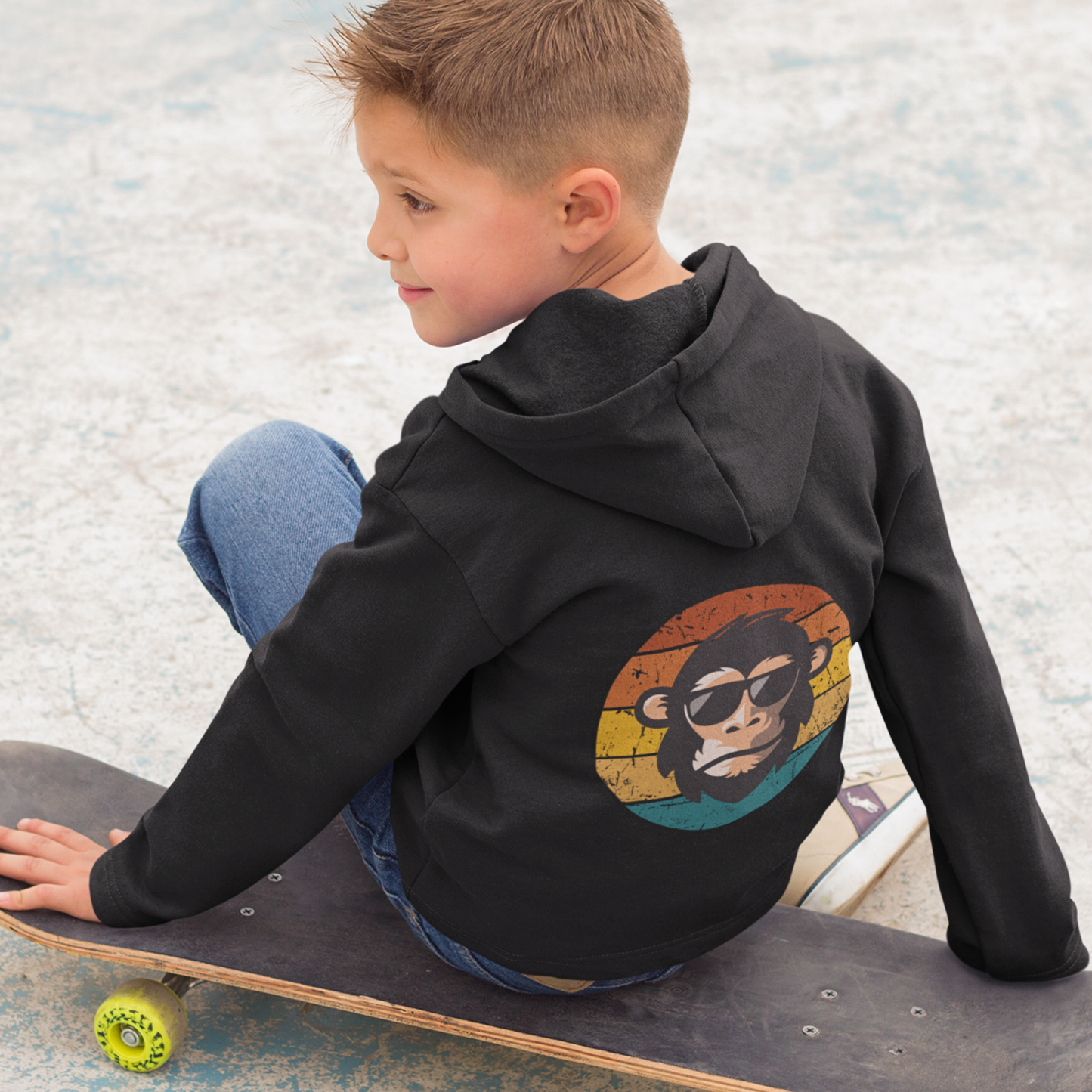 Boy wearing black kids zip hoodie with cool primate back print while sitting on a skateboard