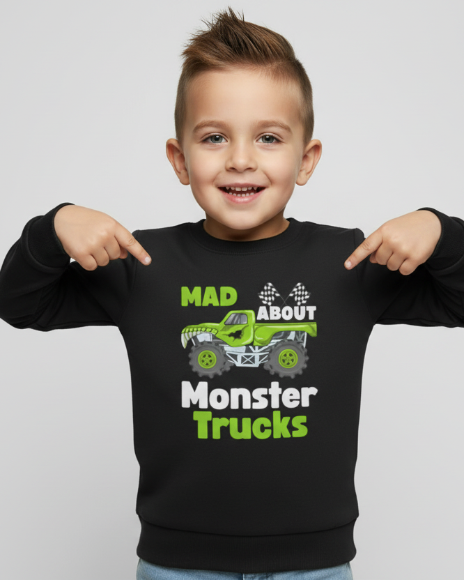 Young boy wearing a black kids sweatshirt with green monster truck graphic and the slogan “Mad About Monster Trucks”, pointing at the design, studio background