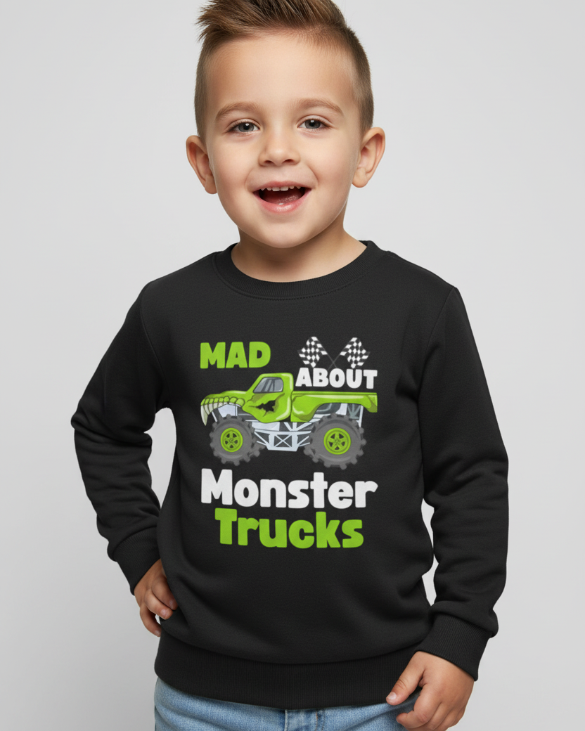 Smiling young boy modelling a black children’s sweatshirt featuring a green monster truck illustration and “Mad About Monster Trucks” text, light studio background