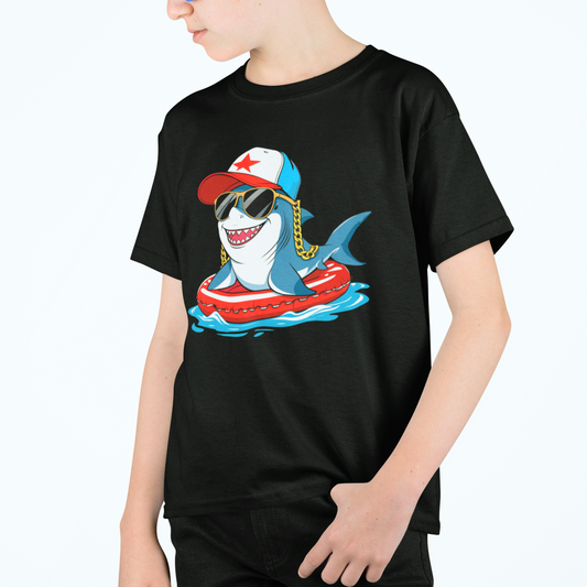 A young boy wearing a black t-shirt with a cartoon shark, the shark is wearing a baseball hat, sunglasses, perched on an inflatable ring
