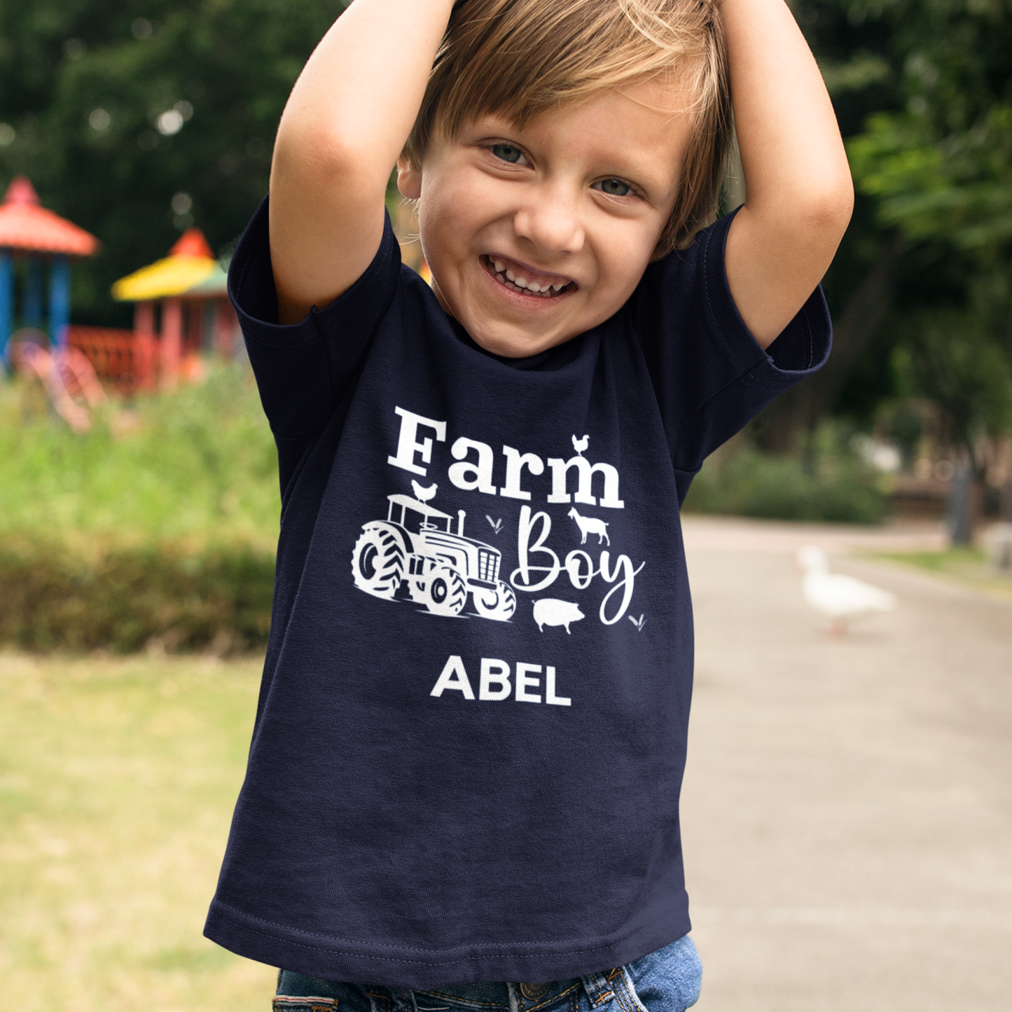 Young boy at the park wearing a printed design, featuring the words "Farm Boy" with tractor and farm animals, with custom name underneath.