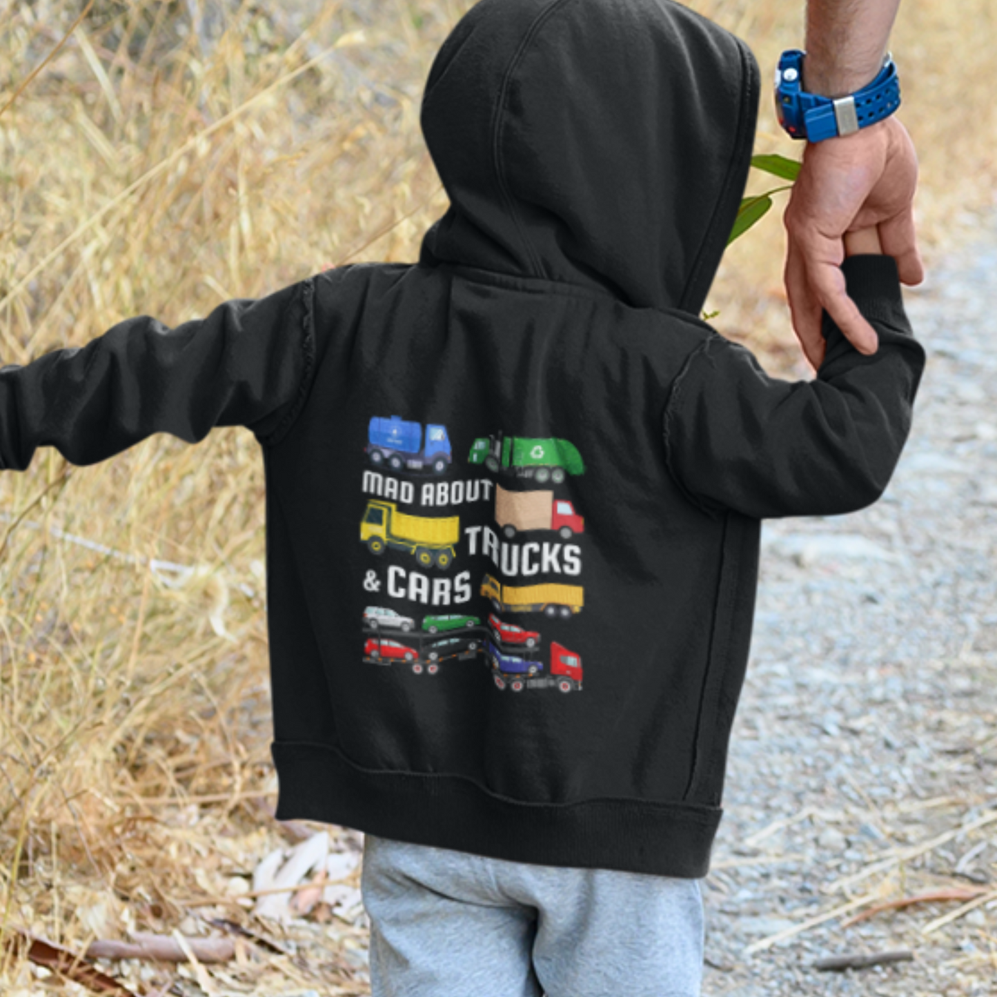 Little boy wearing a black zip hoodie with colourful trucks, transporter and cars design and text 'Mad About Trucks & Cars' printed on the back."