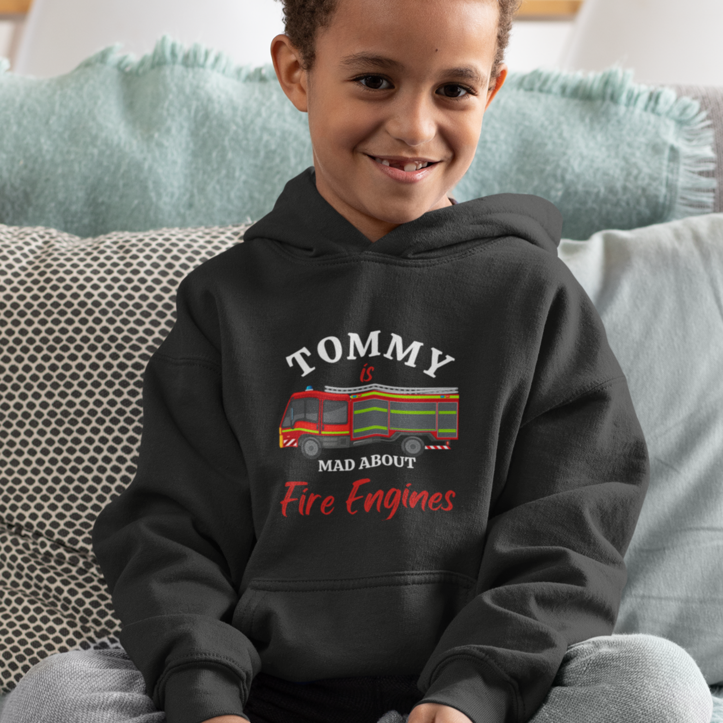 Smiling boy wearing a black personalised Mad About Fire Engines hoodie with a colourful British fire engine graphic and name on the front.