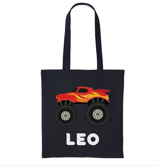Kids black tote bag featuring a red monster truck with flames and the custom name printed in bold white text.