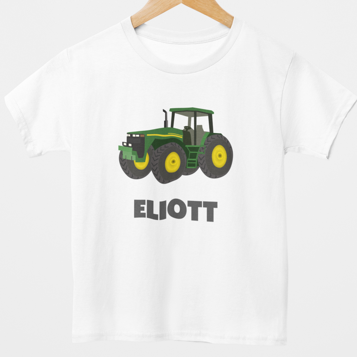 Styled on a wooden hanger; a Kids sized cotton t-shirt with a green tractor and personalised name, printed in bold grey letters on the front.