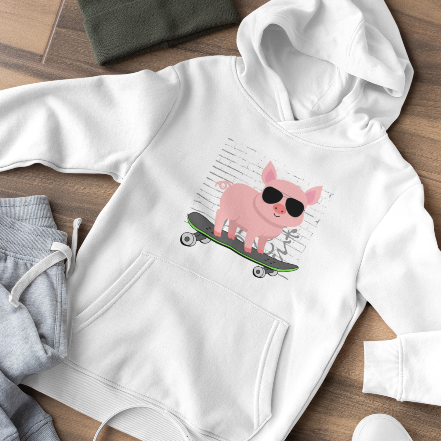 Kids white hoodie with cool skateboarding pig graphic wearing sunglasses, flat lay outfit with grey joggers on wooden floor