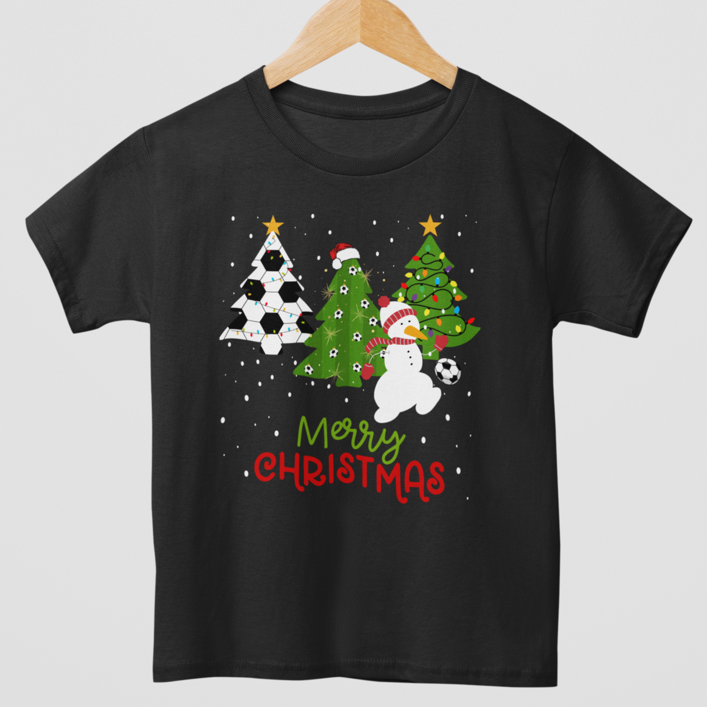 A kids t-shirt with a Christmas theme, featuring footballs, trees, a snowman, and the text 'Merry Christmas'.