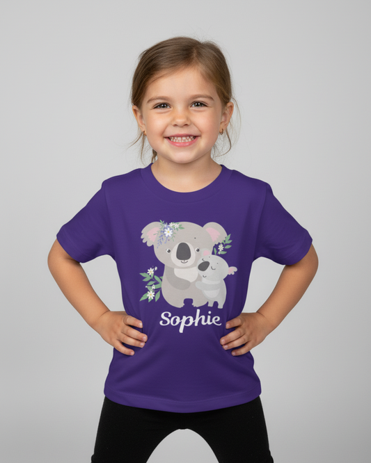 Smiling young girl wearing a purple personalised koala T-shirt with the name Sophie, standing confidently in a studio with a neutral background.
