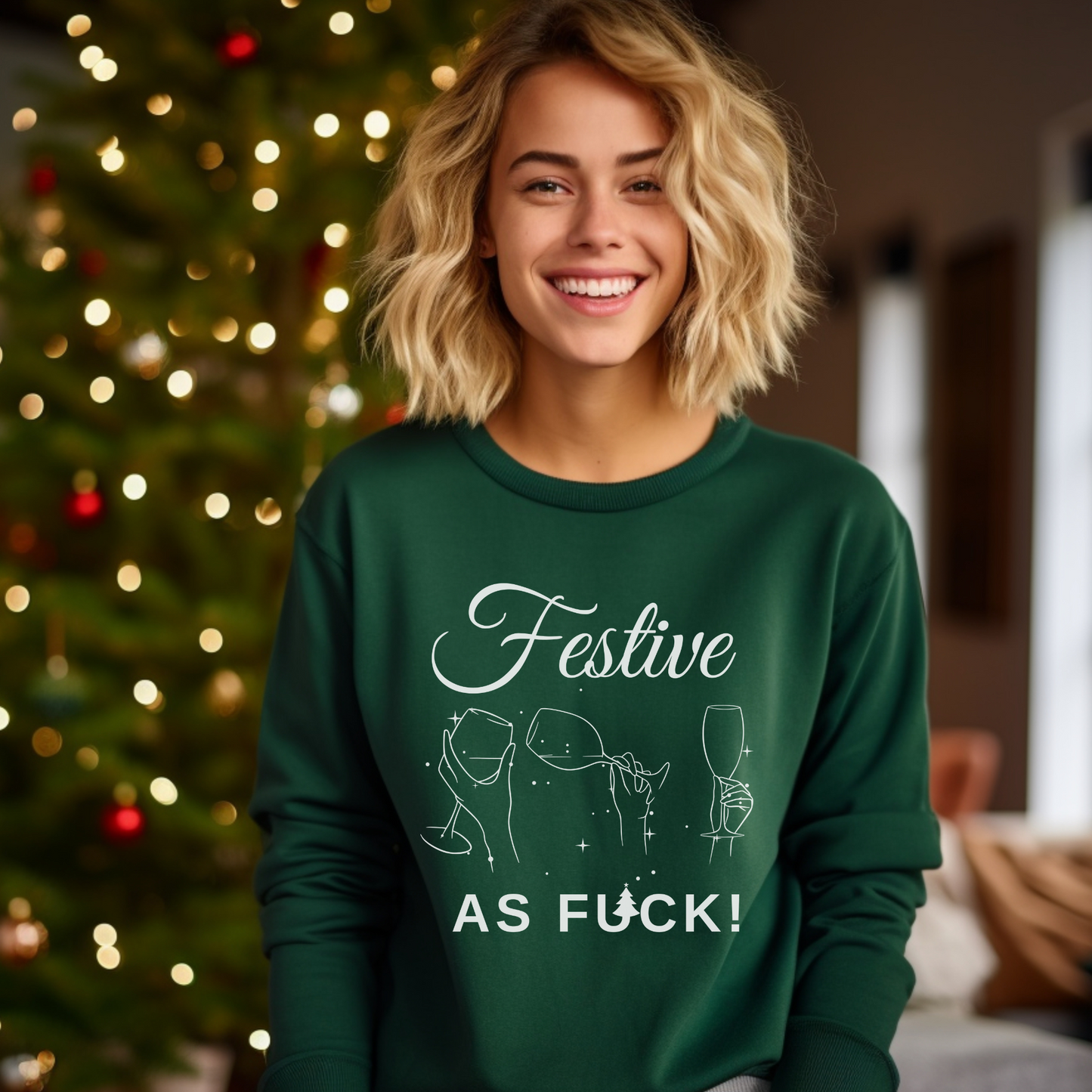 A woman smiling and wearing a green Christmas sweatshirt with the text 'FESTIVE AS F*CK!' on it, standing in front of a blurred Christmas tree and decoration background.