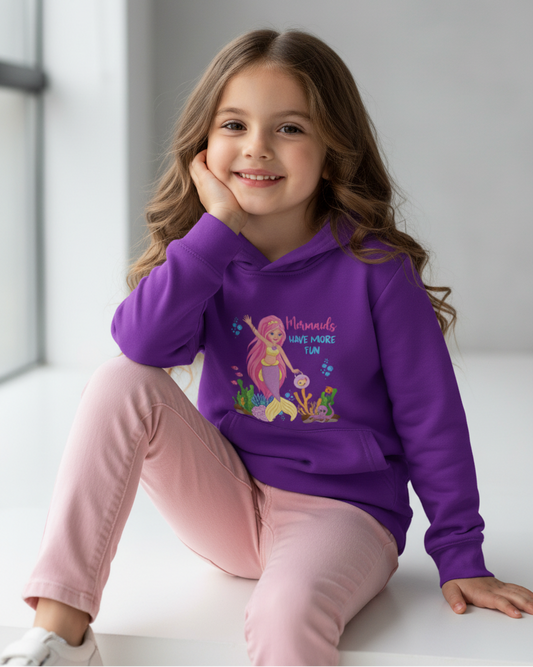 Smiling girl sitting in studio wearing purple “Mermaids Have More Fun” kids hoodie with ocean-themed print