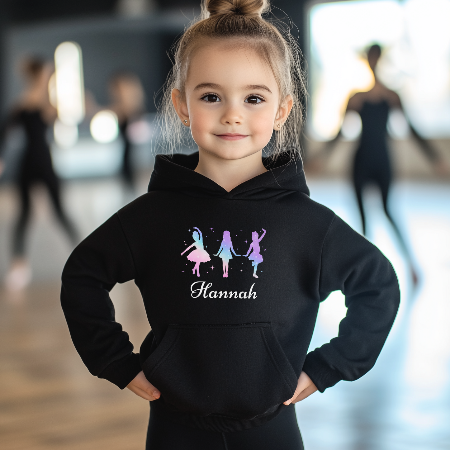 Young girl modelling a black pullover hoodie featuring three colourful dancer silhouettes representing tap, jazz, and ballet styles with a personalised name printed below design