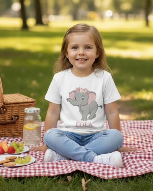 Girls custom name elephant t-shirt in white with flower crown elephant graphic and name “Lola”, picnic lifestyle image in park setting.