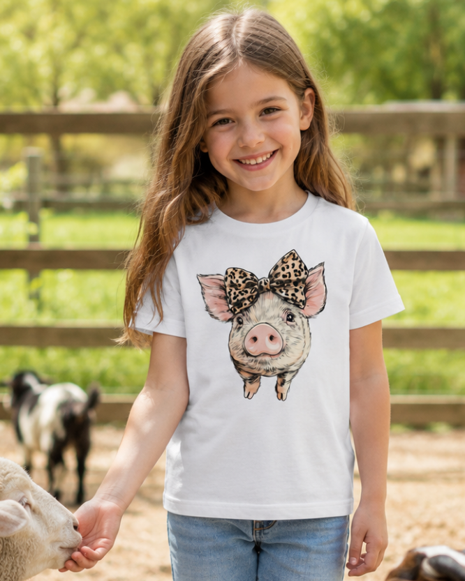 Young girl wearing a white t-shirt with a pig design, standing in a farm setting.
