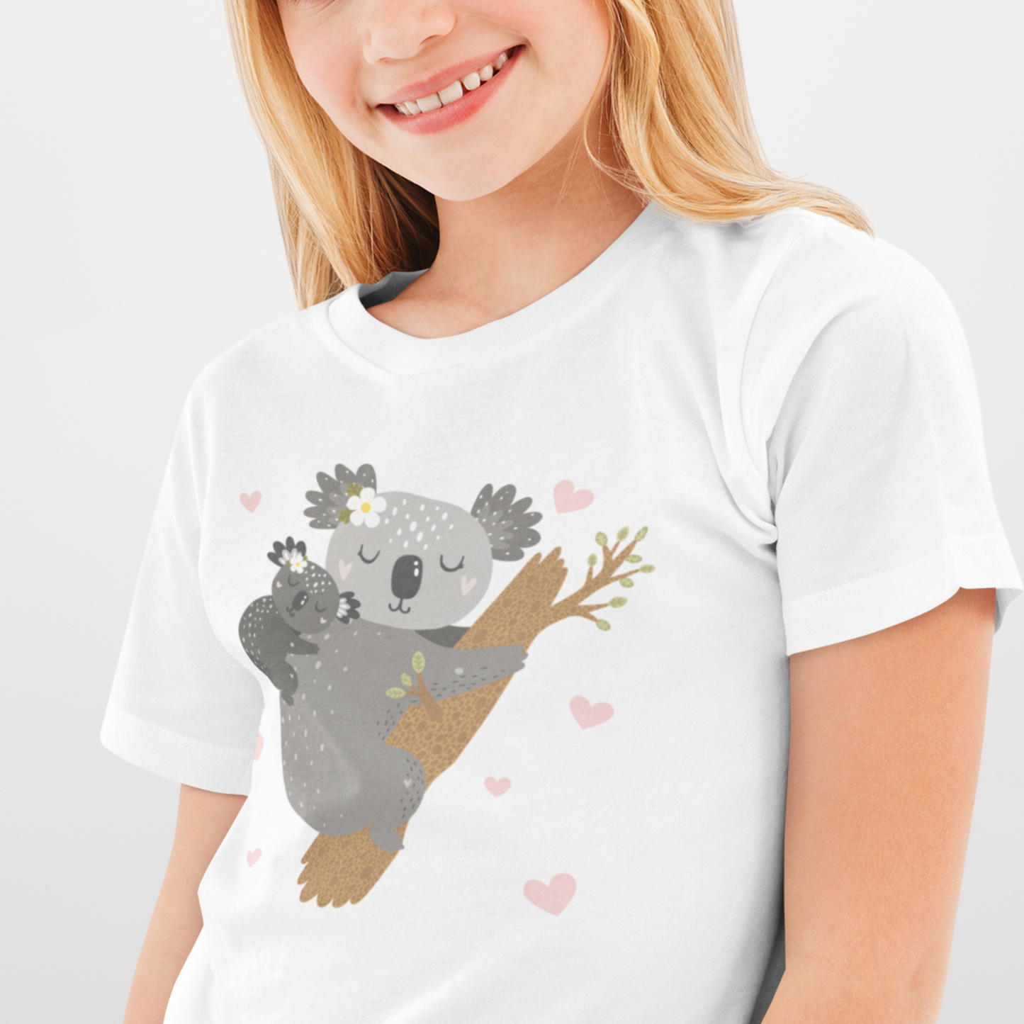 Young girl wearing a white graphic tee featuring an illustration of a mother koala cuddling her baby while clinging to a tree, surrounded by small pink hearts and flowers.