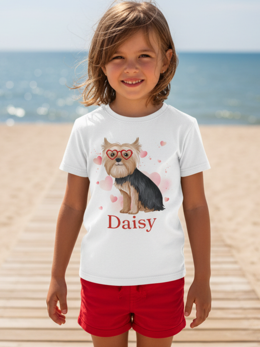 Happy young girl wearing a white personalised Yorkshire Terrier t-shirt with heart glasses dog design and the name Daisy on a sunny beach boardwalk.