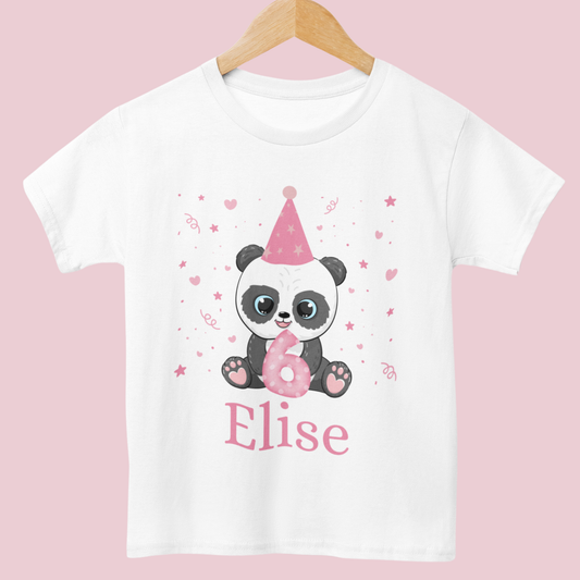White cotton girls birthday t-shirt featuring a cute panda in a pink party hat holding a number with confetti, stars and hearts around, styled on a wooden hanger