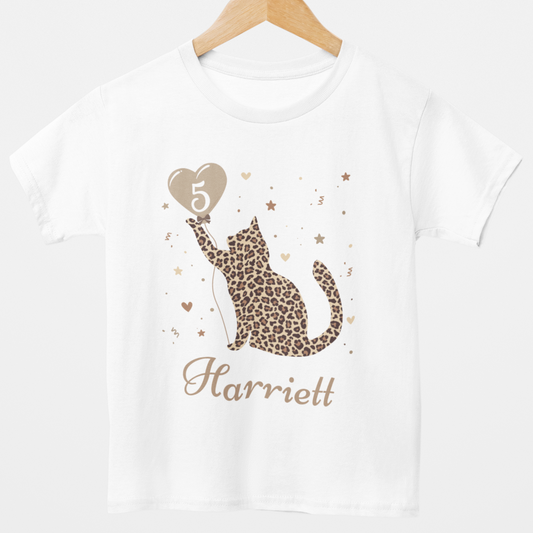 A white t-shirt with a leopard print cat design, hearts, confetti, and a personalized name 'Harriett' printed on the front.