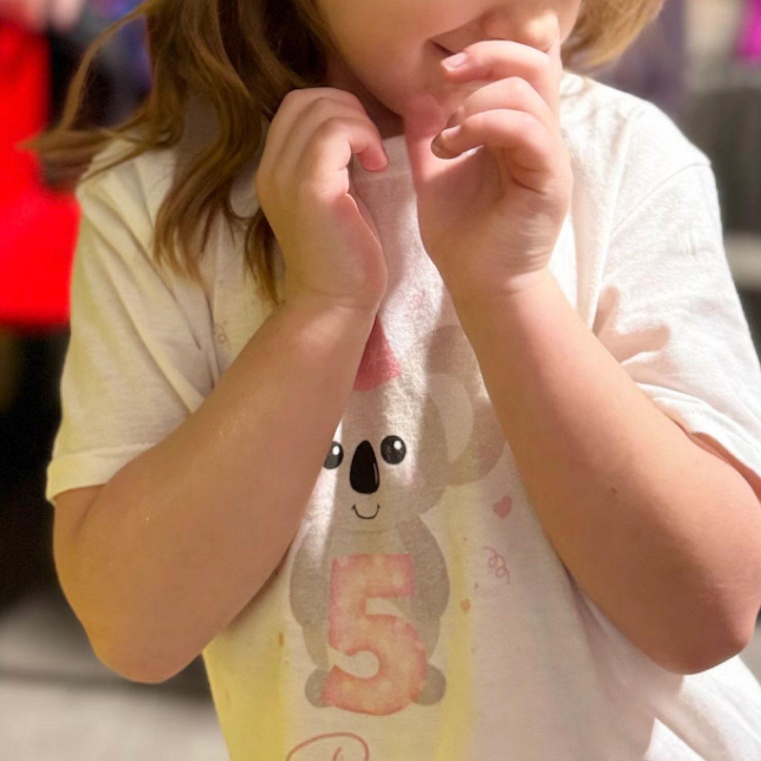 A customers photo of a little girl wearing a white personalised birthday T-shirt, featuring a cute grey koala with a pink party hat, birthday number five with hearts and stars accents.