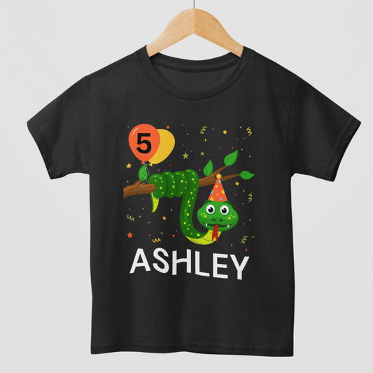Kids black t-shirt with a vibrant illustration of a green snake on a branch with a number 5 and the name 'ASHLEY' printed on it, indicating it's a personalized birthday shirt.