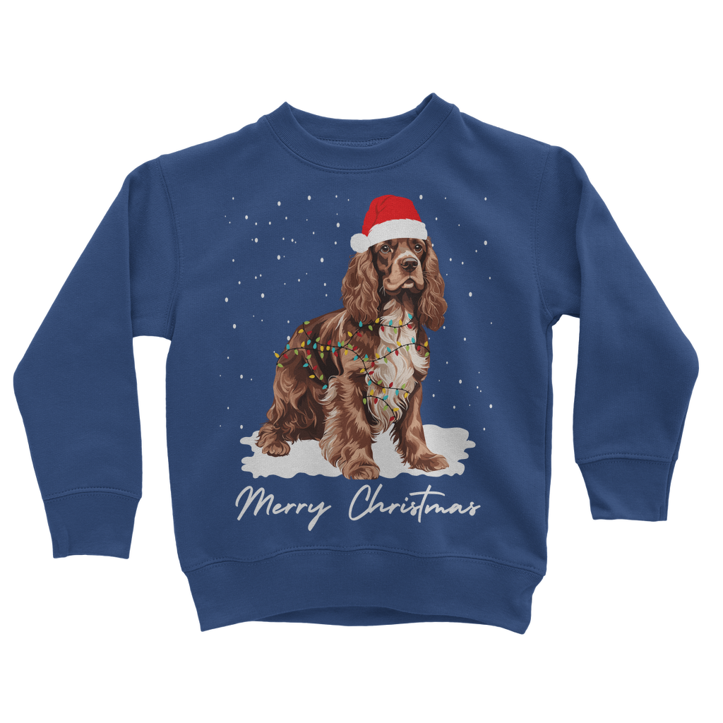 Kids royal blue Christmas sweatshirt featuring a brown and white Cocker Spaniel, wearing Santa hat, wrapped in Xmas lights with falling snow design.