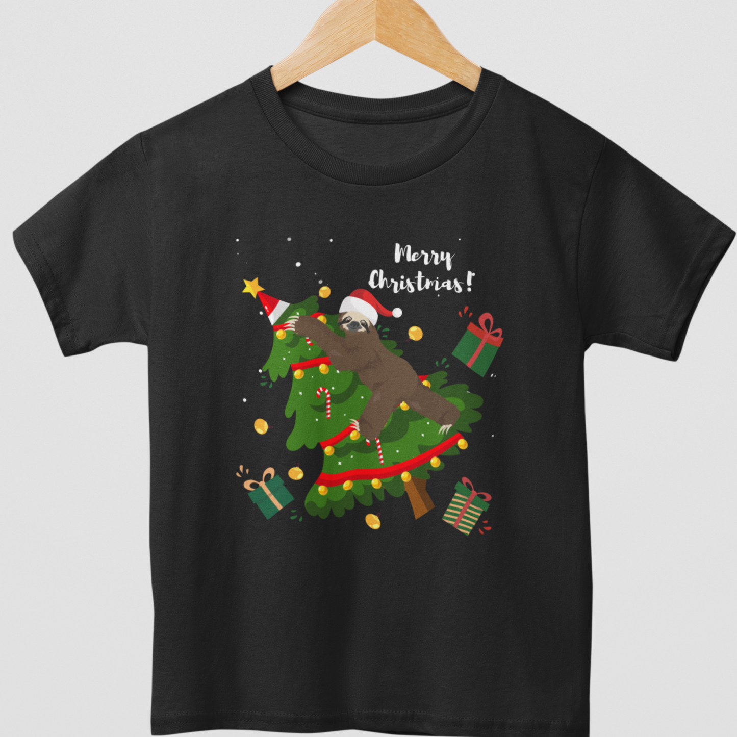 Children's black t-shirt with a graphic of a sloth climbing a Christmas tree, surrounded by festive decorations and the text 'Merry Christmas!' on a wooden hanger