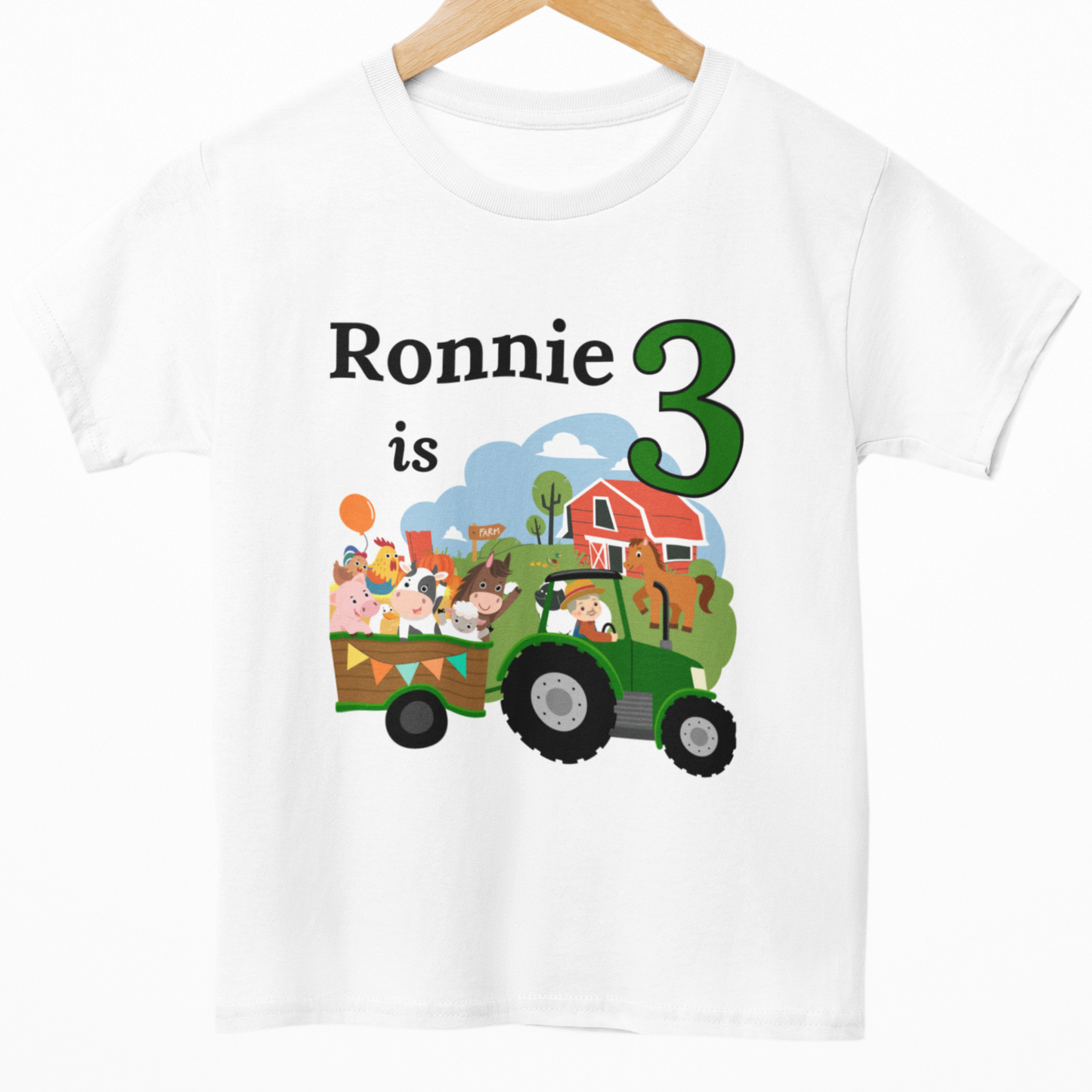 Kids personalised farm themed birthday T-shirt with “Ronnie is 3” and a colourful tractor and happy cartoon animals in a trailer.