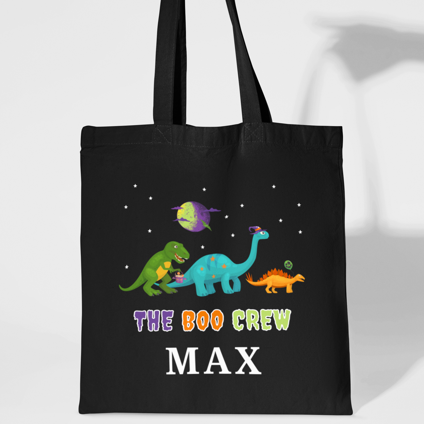Black personalised kids Halloween tote bag featuring colourful cartoon dinosaurs under stars with the text “The Boo Crew” and the name “Max”.