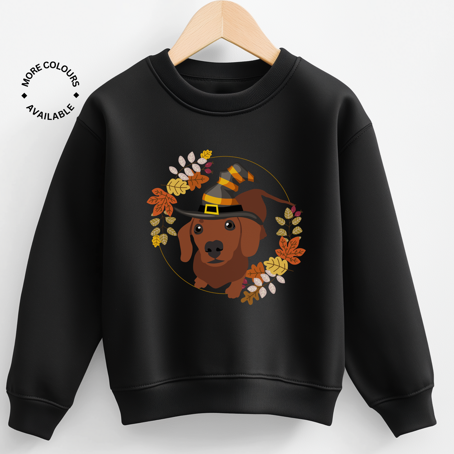 Kids black sweatshirt on a hanger featuring a cute dachshund wearing a witch hat, surrounded by autumn leaves in warm fall colours.