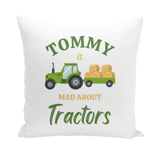 A white square cushion cover featuring a green cartoon tractor pulling a trailer loaded with hay bales. Above the tractor, the name "TOMMY" is displayed, and below the tractor, the text "MAD ABOUT Tractors" is shown.