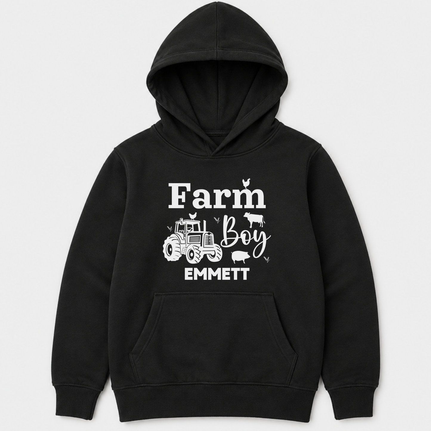 A kids black pullover hoodie with a white graphic print on the front that reads 'Farm Boy EMMETT' with a tractor and small farm animal illustrations, shown on a light grey background.