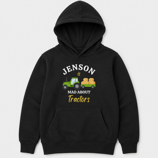 Children's black pullover hoodie with a front graphic that reads 'JENSON IS MAD ABOUT Tractors' in white and yellow text, featuring a small green tractor and hay bale illustration, shown on a light grey background.