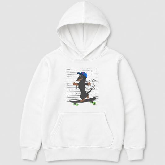 A kids white pullover hoodie featuring a cartoon graphic of a dachshund wearing a blue cap and riding a skateboard against a background of printed text, shown on a light grey studio background.