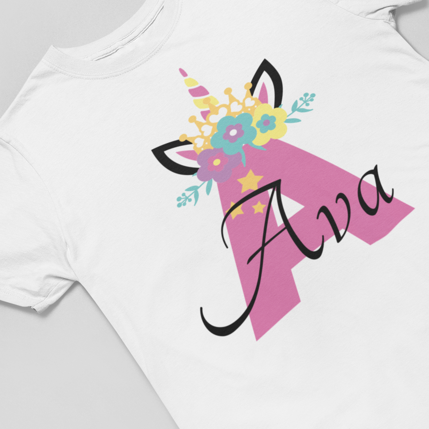 Kids white t-shirt featuring a pink unicorn horn and ears design with colourful floral crown and stars. Personalised with a large 'A' initial and custom name 'Ava'