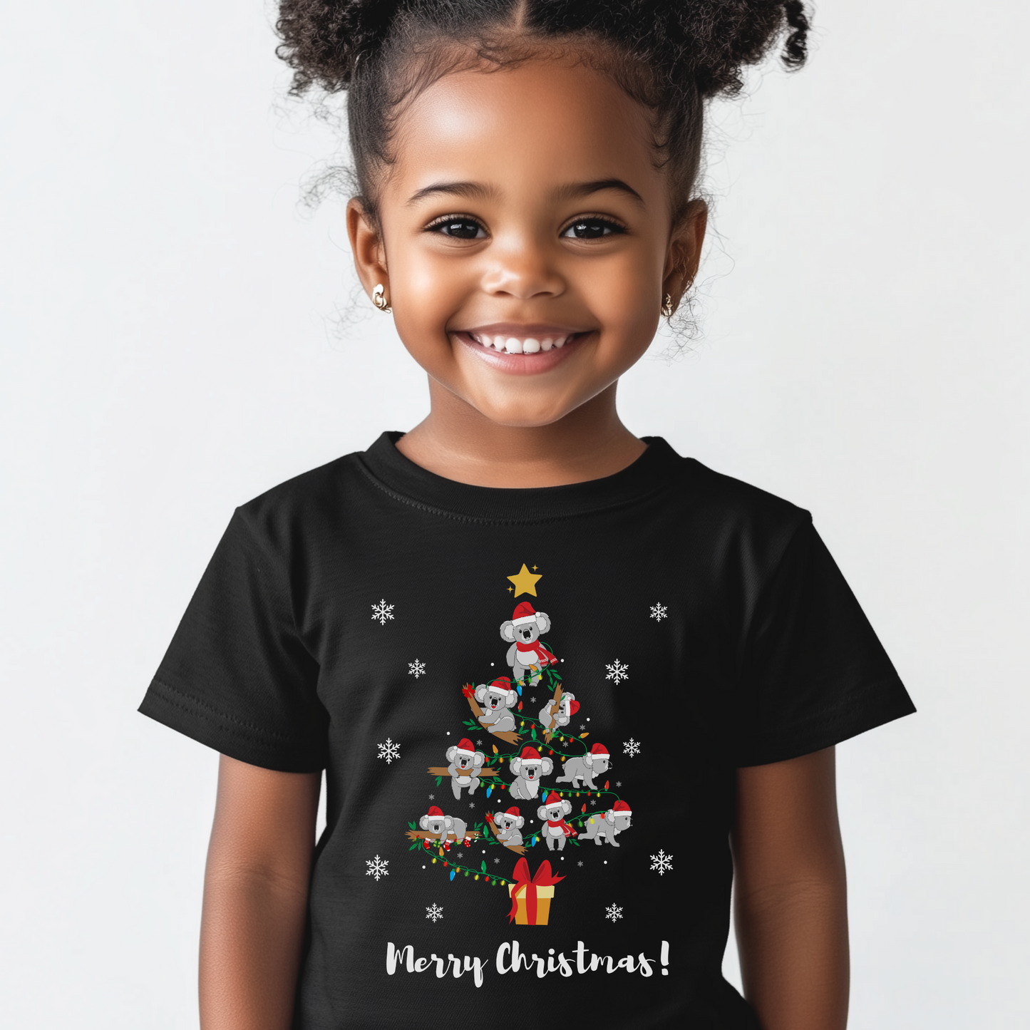 Young girl wearing a black Christmas T-shirt featuring an adorable design of multiple koalas forming the shape of a Christmas tree, with festive lights, snowflakes, and a gift box at the bottom, and the text “Merry Christmas!” below.