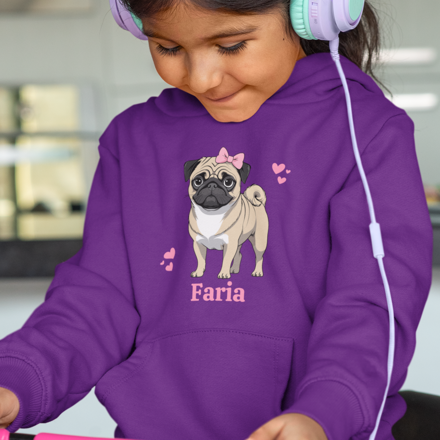 Young girl is wearing a purple hoodie with a pug with a pink bow and hearts design and her name 'Faria' printed underneath the dog.