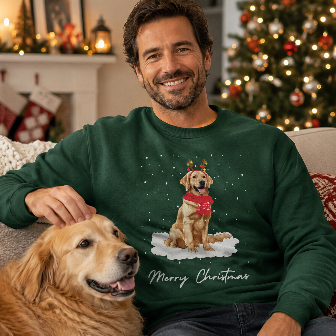 A man wearing a dark green Christmas crewneck sweatshirt with a graphic of a golden retriever dog wearing a red scarf in the snow, sitting on a couch next to a golden retriever dog in a cozy living room with a decorated Christmas tree in the background.