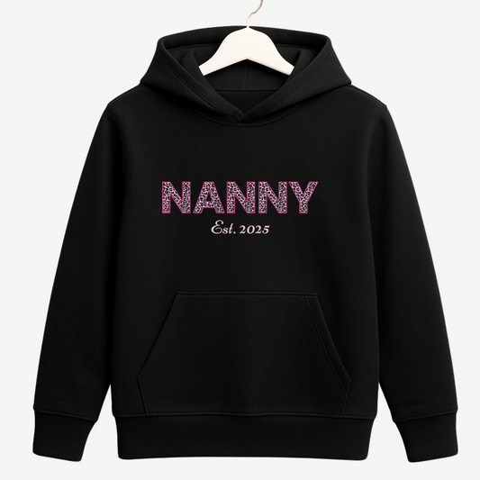 Women's black pullover hoodie with Leopard print 'NANNY Est. 2025' on a wooden hanger