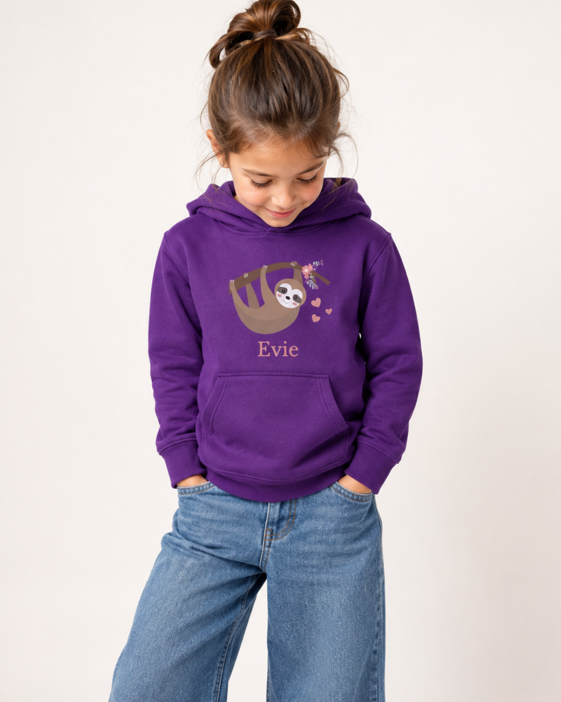 Girl wearing a purple personalised sloth hoodie featuring a smiling sloth hanging from a branch with pink flowers and hearts, with the name Evie printed underneath