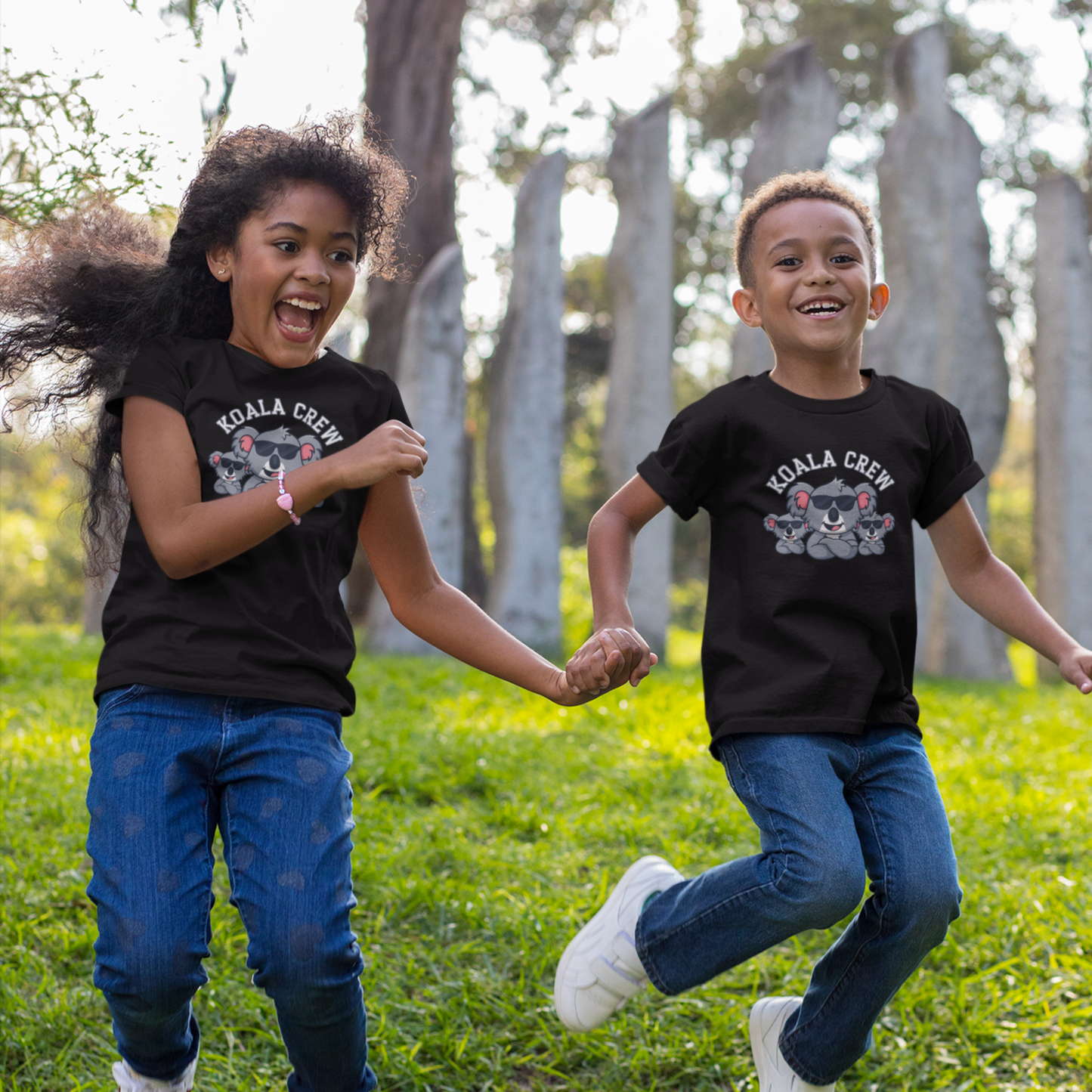 Two children running together in a grassy area wearing black t-shirts with koala designs.