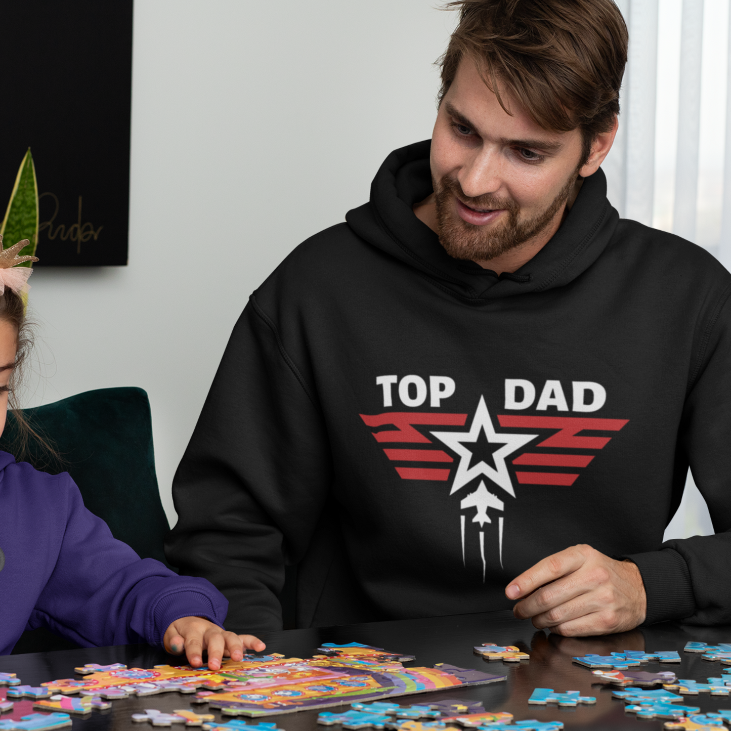 Man wears a black pullover hoodie with 'TOP DAD' text and a star and fighter jet graphic on the front.