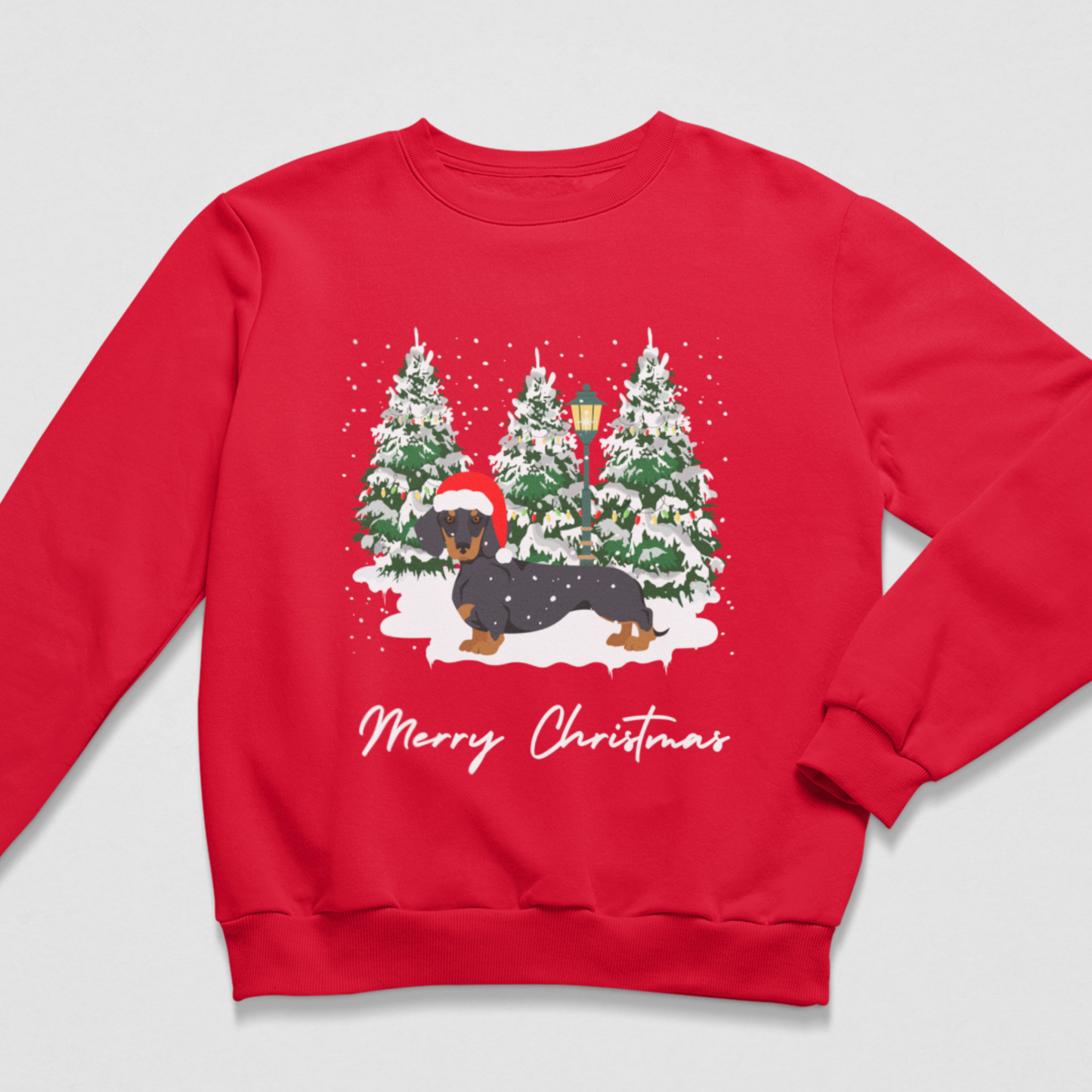 A red crewneck sweatshirt featuring a festive Christmas graphic of a dachshund in a snowy winter scene with pine trees and the text 'Merry Christmas' printed below.