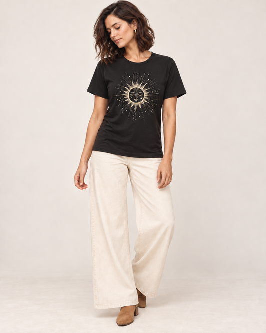 Woman wearing a black celestial sun and moon T-shirt with cream wide-leg trousers and tan ankle boots in a bright studio.