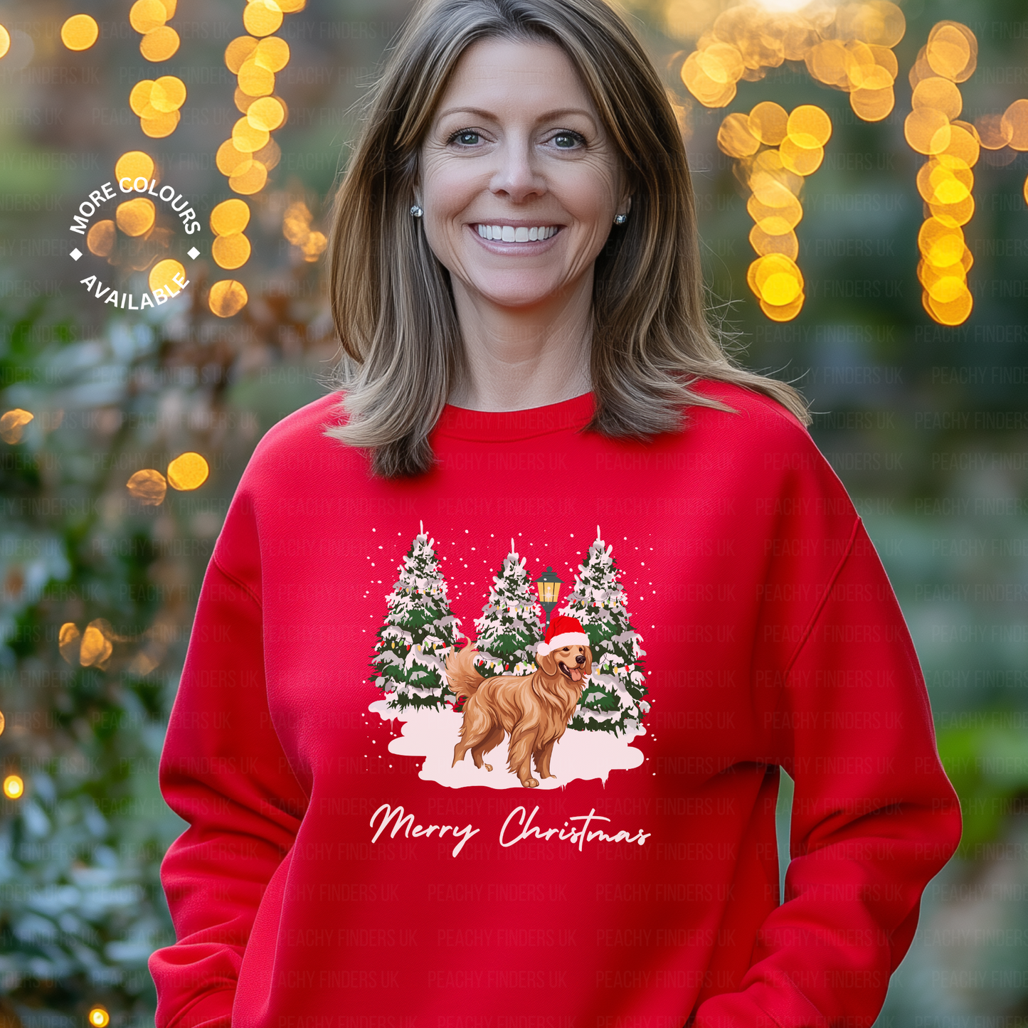 Woman wearing red Christmas sweatshirt with golden retriever in Santa hat design, standing in front of snowy pine trees and “Merry Christmas” text.