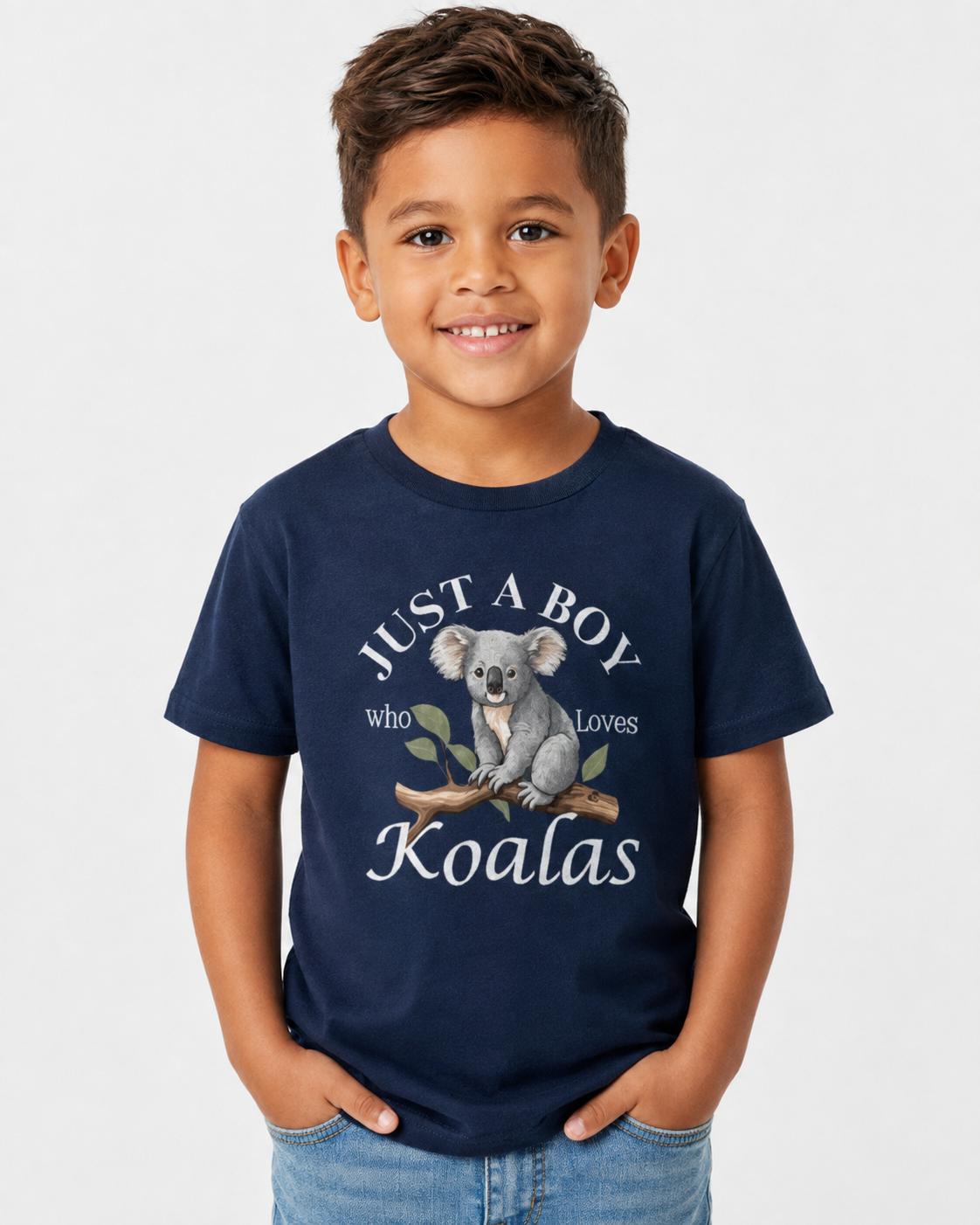 A young boy smiling and wearing a navy blue graphic t-shirt with a koala design and the text 'JUST A BOY who loves Koalas', paired with light blue jeans, against a plain light gray background.