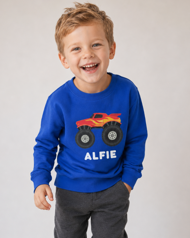 Happy boy wearing a blue sweatshirt with a red and yellow monster truck graphic custom name 'ALFIE' - studio setting