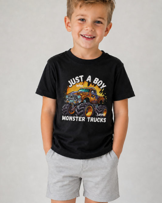 Young boy wearing a black monster truck T-shirt with light grey shorts, featuring a “Just A Boy Who Loves Monster Trucks” graphic.